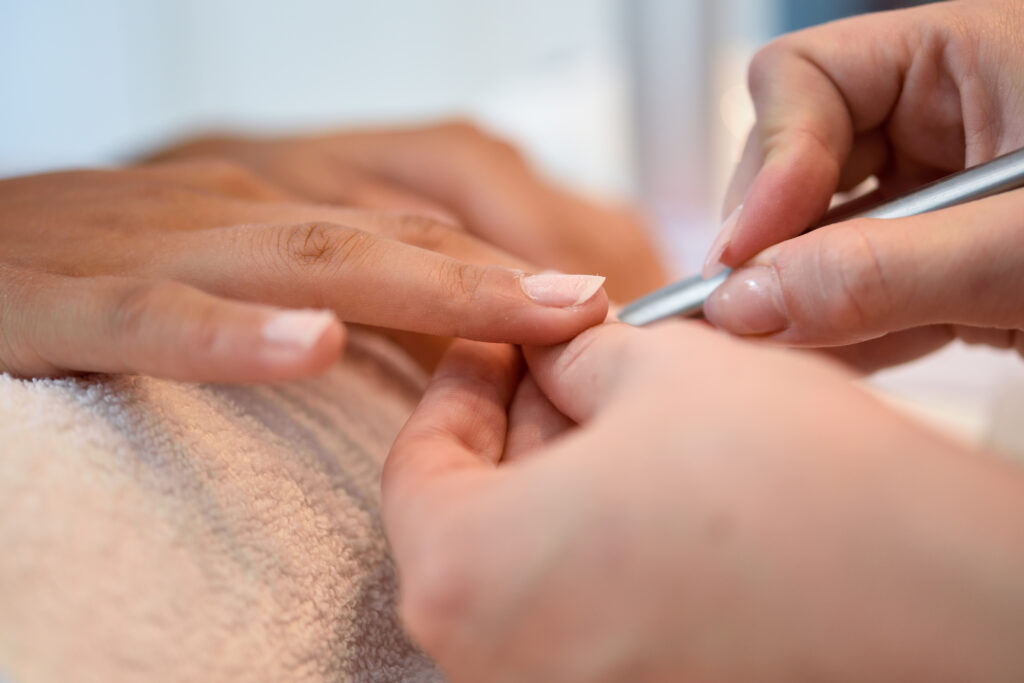 Mulher e homem com unhas deterioradas recebendo manicure de uma esteticista com lixa de unha.